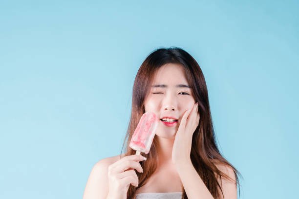 Asian woman hold popsicle have a hypersensitive teeth on the blue background